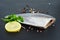 Ready-to-cook raw fresh pompano fish, lemon slice, spices, sauce and parsley on a black stone slate