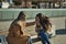 Real couple of young women, holding hands, sitting on a bench, while one kisses the other on the hand in an affectionate attitude