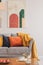 Real photo of an abstract painting hanging on white wall in living room interior with colorful cushions on gray sofa