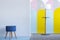 Real photo of a blue stool and a modern lamp in bright living room interior with colorful arches on the white wall. Place for you