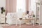 Real photo of bright provencal sitting room interior with white sofa, wooden coffee table on dirty pink carpet, rack with decor an