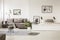 Real photo of a grey sofa standing next to a bed in monochromatic, spacious room interior with lamps, posters, rug and plant