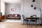 Real photo of metal lamp standing next to dining table with two black chairs in open space flat interior with leather couch. moder