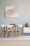 Real photo of a natural, scandi dining room interior with a round, wooden table and white chairs standing against light gray wall