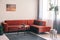 Real photo of a red, suede sofa standing in the corner of a bright living room interior with plants on a swing