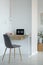 Real photo of a simple home office interior with a laptop on a wooden desk and a gray chair