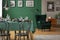 Real photo of a table with green cloth and black chairs in blurred foreground and a comfy armchair in the background in dining