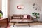 Real photo of wooden coffee table placed on carpet in bright sitting room interior with leather brown couch, modern clock on wall,