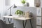 Real photo of wooden desk with fresh plant, black lamp, coffee c