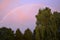 Real photograph of a rainbow over trees in front of a pink colored sky.