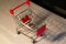 Realistic iron mini shopping cart with red plastic parts on top of a computer keyboard. Object for purchases such as sales