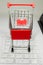 Realistic iron mini shopping cart with red plastic parts on top of a computer keyboard. Object for purchases such as sales