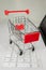 Realistic iron mini shopping cart with red plastic parts on top of a computer keyboard. Object for purchases such as sales