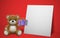 Realistic little cute smiling baby bear doll character holding a present gift and sitting on white frame with red background. An a