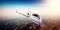 Realistic photo of white generic design private Jet flying over the mountains. Empty blue sky with sun at background