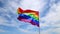 Realistic rainbow flag of an LGBT organization waving against a blue sky, clouds . LGBT pride flags include lesbians