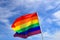 Realistic rainbow flag of an LGBT organization waving against a blue sky. LGBT pride flags include lesbians, gays