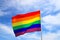 Realistic rainbow flag of an LGBT organization waving against a blue sky. LGBT pride flags for lesbians, gays, bisexuals and