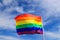 Realistic rainbow flag of an LGBT organization waving in blue sky. LGBT pride flags include lesbians, gays, bisexuals and