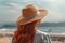 Rear back view ginger haired lady in straw hat enjoying summer day by sea shore. AI generative