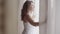 Rear back view at rich mature woman opening curtain lace standing in luxury apartment home or modern hotel looking