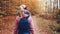 Rear close up view of woman with blue backpack and lilac hiking jacket walking on the autumn forest path trail