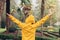 Rear image of a person with yellow raincoat and open arms, screaming in the rain in nature. Concept of feeling of freedom, relief