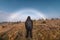 Rear of male traveler adventure standing on golden meadow with fog bow or white rainbow on autumn forest in Assiniboine provincial