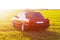 The rear of the old, red, German car that stands on the grass during sunset