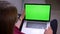 Rear portrait of businesswoman in glasses watching into laptop attentively with green chroma screen at home.