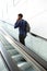 Rear portrait of man standing on escalator talking on smart phone