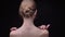 Rear portrait of young and slim caucasian girl touching softly her neck and back on black background.