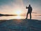 Rear silhouette of travelling man taking selfie at sea. Tourist with backpack standing on a rock