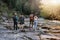 Rear on two couples standing hand in hand at river on rocks. Hikers in mountains valley.