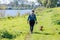 Rear view of adult female hiker walking on green grass with her brown dachshund