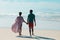 Rear view of african american young man holding girlfriend\\\'s hands and walking at beach against sky