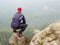 Rear view of alone hiker in dark outdoor suit sit on the edge. Sharp rocky peak above mountains valley