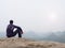 Rear view of alone hiker in dark outdoor suit sit on the edge. Sharp rocky peak above mountains valley