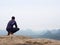 Rear view of alone hiker in dark outdoor suit sit on the edge. Sharp rocky peak above mountains valley