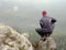 Rear view of alone hiker in dark outdoor suit sit on the edge. Sharp rocky peak above mountains valley