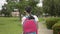 Rear view of asian elementary schoolgirl in protective face mask wearing headphones and walking at public park.
