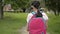 Rear view of asian elementary schoolgirl in protective face mask wearing headphones and walking at public park.