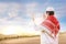 Rear view of asian muslim man with cap and turban standing and praying with raised arms on the sand