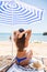 Rear view of Attractive woman with tanned skin posing at beach in sunny day. Portrait from back of stylish girl in blue bikini sit