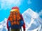 Rear view of a backpacker hidden behind the huge backpack. Mountain hiker stands in front of the snowy mount on sunny day. Low