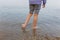 rear view of barefeet child legs standing in the water in stone beach in striped pants