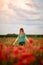 Rear view of beautiful young woman with long hair who standing on field with red poppies.