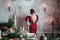 Rear view beautifull young woman stands against grey wall in red dress near served table with candles and fir branches