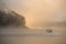 rear view of boat quickly floating on the water against the backdrop of silhouette of hill in fog