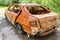 Rear view of burnt rusty passenger car on a summer day